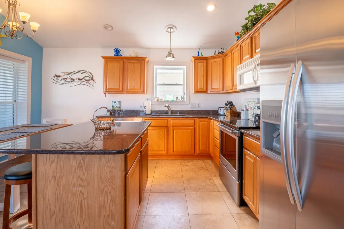 A bright, inviting kitchen with a spacious island and stainless steel appliances. Wooden cabinets and decorative shelves add warmth, creating the perfect spot for casual gathering and meal prep. The kitchen opens toward the living space, bathed in natural light.