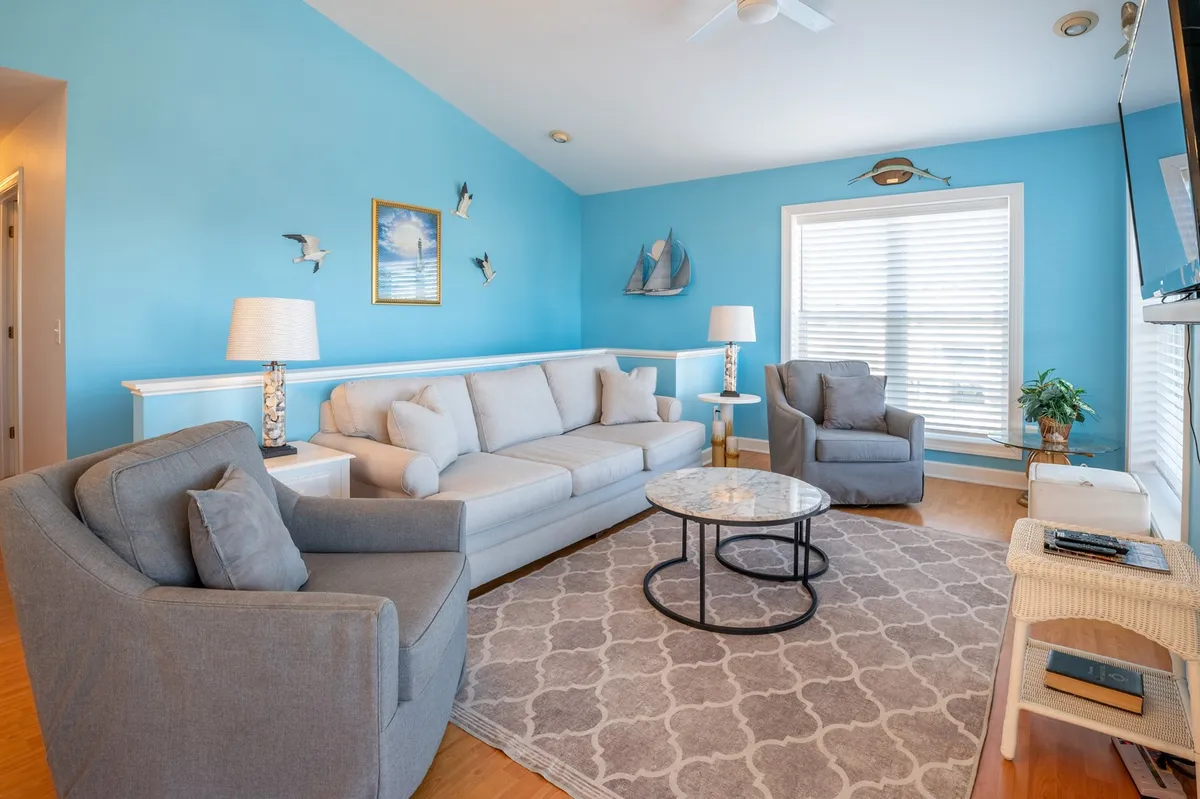 A spacious, comfortable living area featuring a sofa, chairs, coffee table, and decorative wall art, bathed in natural light. The layout encourages socializing, relaxing, and enjoying time indoors in any season.