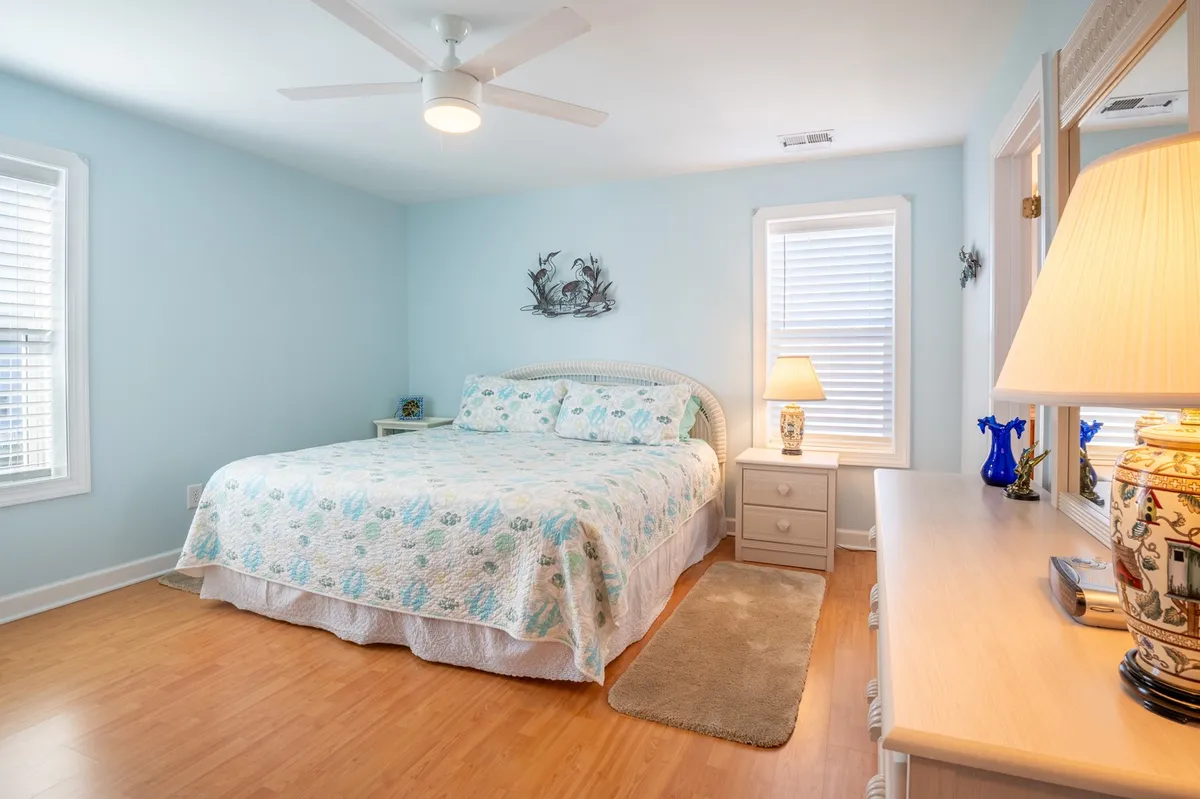 A serene bedroom featuring a comfortable bed, a nightstand with a lamp for evening reading, decorative wall art, and a dresser. The space emits a peaceful ambiance, ideal for unwinding after a day in the sun.
