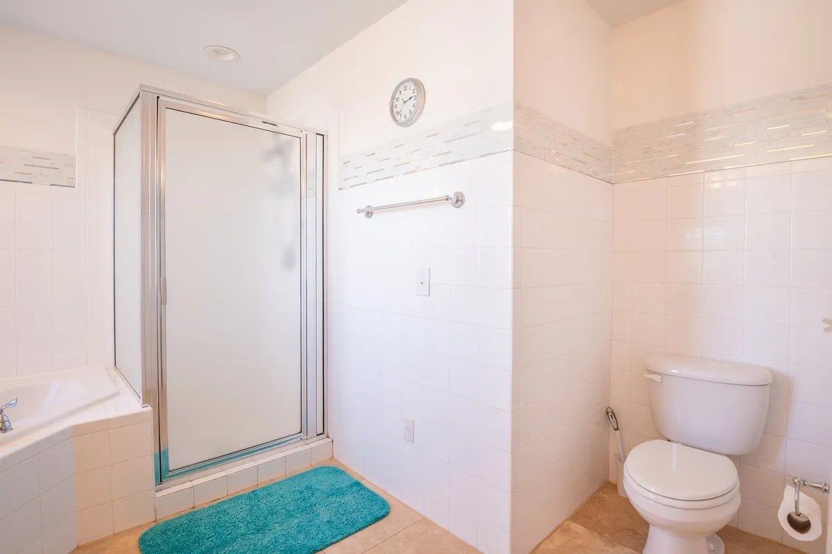 A serene bathroom with a glass-enclosed shower, bathtub, towel rack, and toilet, all in a calming, neutral palette. The space suggests ease of use and rejuvenation after a day at the beach.