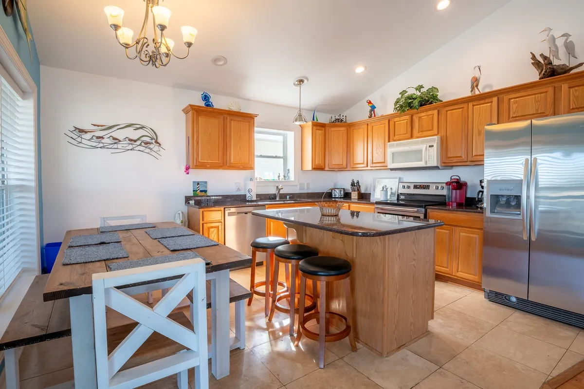 A spacious kitchen and dining area with a central island, wooden cabinetry, modern appliances, and a large dining table. Decorative accents add warmth, and ample space invites group cooking and shared meals.